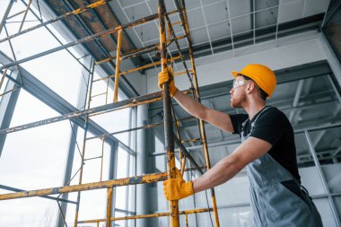 Man in grey uniform works with construction indoors in modern big office at daytime.