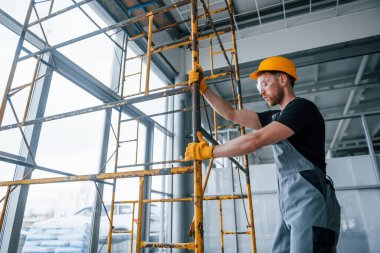 Man in grey uniform works with construction indoors in modern big office at daytime.
