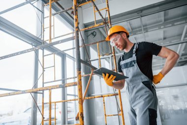 Engineer in grey uniform with notepad in hands works indoors in modern big office at daytime.