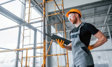 Engineer in grey uniform with notepad in hands works indoors in modern big office at daytime.