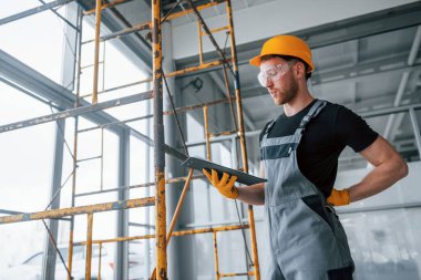 Engineer in grey uniform with notepad in hands works indoors in modern big office at daytime.