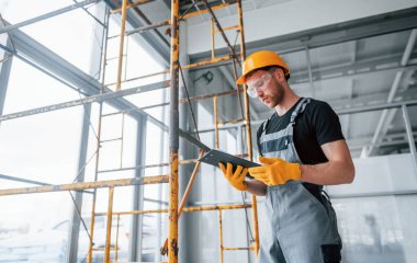 Engineer in grey uniform with notepad in hands works indoors in modern big office at daytime.