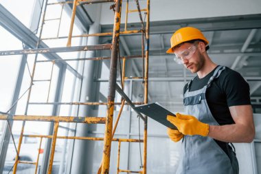 Engineer in grey uniform with notepad in hands works indoors in modern big office at daytime.