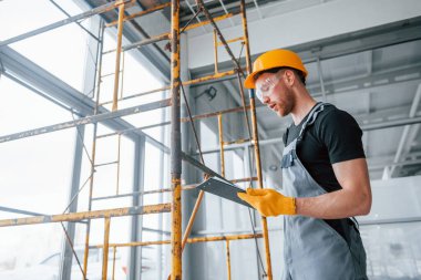 Engineer in grey uniform with notepad in hands works indoors in modern big office at daytime.