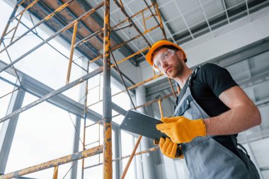 Elinde not defteri olan gri üniformalı bir mühendis modern büyük ofiste gündüzleri kapalı bir yerde çalışıyor..