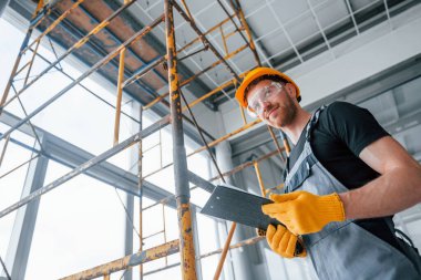 Engineer in grey uniform with notepad in hands works indoors in modern big office at daytime.