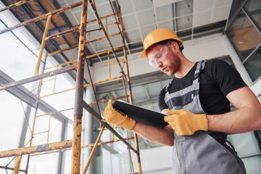 Engineer in grey uniform with notepad in hands works indoors in modern big office at daytime.