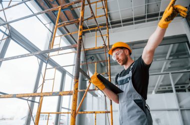 Engineer in grey uniform with notepad in hands works indoors in modern big office at daytime.