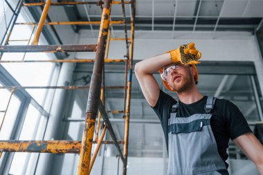 Gri üniformalı mühendis gündüz vakti modern büyük ofiste kapalı bir yerde mola veriyor..