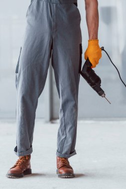 Gri üniformalı, elinde matkapla modern büyük ofiste gündüz vakti elinde matkapla gezen adamı yakından izle..