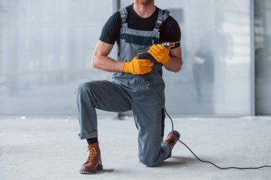 Gri üniformalı, elinde matkapla modern büyük ofiste gündüz vakti elinde matkapla gezen adamı yakından izle..