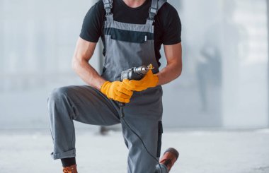 Gri üniformalı, elinde matkapla modern büyük ofiste gündüz vakti elinde matkapla gezen adamı yakından izle..