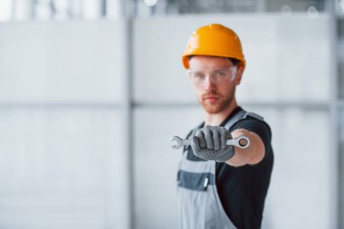 Gri üniformalı, elinde İngiliz anahtarı olan bir adam. Gündüz vakti modern büyük ofiste kapalı duruyor..