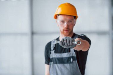 Gri üniformalı, elinde İngiliz anahtarı olan bir adam. Gündüz vakti modern büyük ofiste kapalı duruyor..