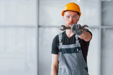 Gri üniformalı, elinde İngiliz anahtarı olan bir adam. Gündüz vakti modern büyük ofiste kapalı duruyor..