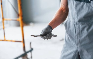 Gri üniformalı, elinde ingiliz anahtarıyla modern büyük ofiste gündüz vakti kapalı duran adamı yakından izle..