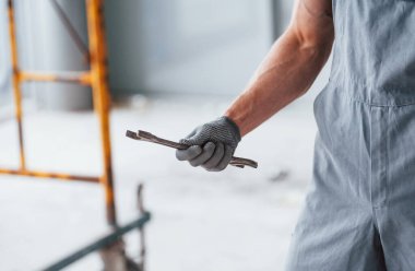 Gri üniformalı, elinde ingiliz anahtarıyla modern büyük ofiste gündüz vakti kapalı duran adamı yakından izle..