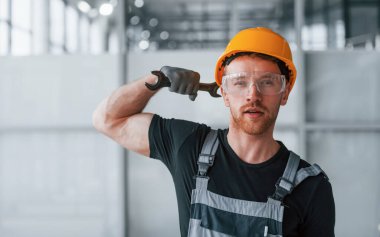 Gri üniformalı, elinde İngiliz anahtarı olan bir adam. Gündüz vakti modern büyük ofiste kapalı duruyor..