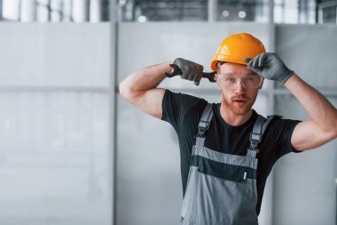 Gri üniformalı, elinde İngiliz anahtarı olan bir adam. Gündüz vakti modern büyük ofiste kapalı duruyor..