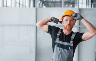 Gri üniformalı, elinde İngiliz anahtarı olan bir adam. Gündüz vakti modern büyük ofiste kapalı duruyor..