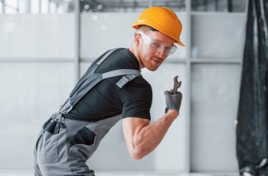 Gri üniformalı, elinde İngiliz anahtarı olan bir adam. Gündüz vakti modern büyük ofiste kapalı duruyor..