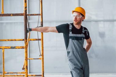 Gri üniformalı bir adam inşaatın yanında duruyor. Gündüz vakti modern büyük ofiste..