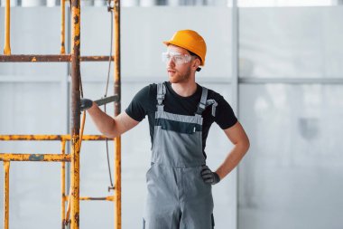 Gri üniformalı bir adam inşaatın yanında duruyor. Gündüz vakti modern büyük ofiste..