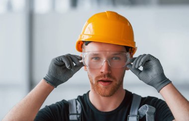 Gri üniformalı, koruyucu gözlüklü ve turuncu şapkalı bir adamın portresi..