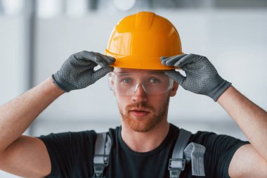 Gri üniformalı, koruyucu gözlüklü ve turuncu şapkalı bir adamın portresi..