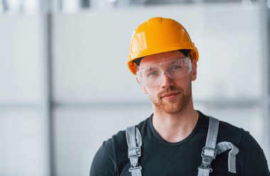 Gri üniformalı, koruyucu gözlüklü ve turuncu şapkalı bir adamın portresi..