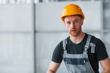 Gri üniformalı ve turuncu şapkalı bir adamın portresi. Gündüz vakti modern büyük ofiste kapalı duruyor..