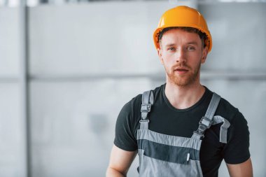 Gri üniformalı ve turuncu şapkalı bir adamın portresi. Gündüz vakti modern büyük ofiste kapalı duruyor..