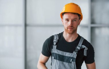 Gri üniformalı ve turuncu şapkalı bir adamın portresi. Gündüz vakti modern büyük ofiste kapalı duruyor..