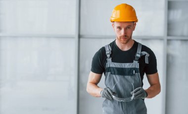 Gri üniformalı ve turuncu şapkalı bir adamın portresi. Gündüz vakti modern büyük ofiste kapalı duruyor..