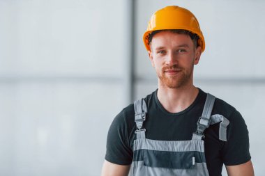 Gri üniformalı ve turuncu şapkalı bir adamın portresi. Gündüz vakti modern büyük ofiste kapalı duruyor..