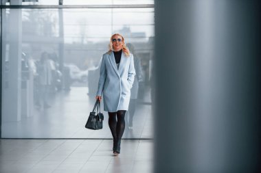 Gri arka planda siyah çantalı şık elbiseli güzel bir sarışın..