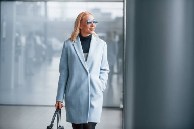 Gri arka planda siyah çantalı şık elbiseli güzel bir sarışın..