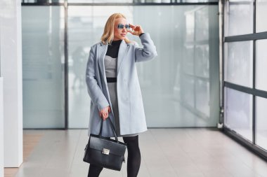 Gri arka planda siyah çantalı şık elbiseli güzel bir sarışın..