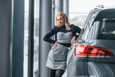 Yeni modern arabanın yanında duran zarif elbiseli güzel sarışın..