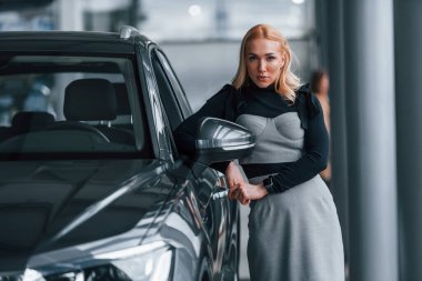 Yeni modern arabanın yanında duran zarif elbiseli güzel sarışın..