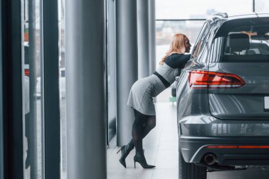 Yeni modern arabanın yanında duran zarif elbiseli güzel sarışın..