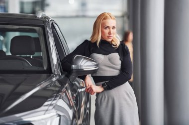 Yeni modern arabanın yanında duran zarif elbiseli güzel sarışın..