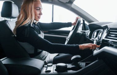 Side view of beautiful blonde in elegant clothes that sitting inside of modern car.