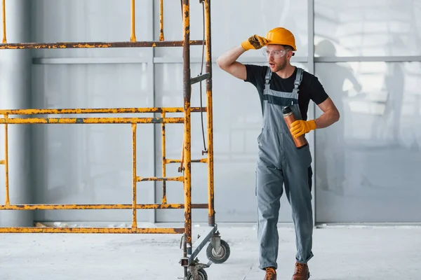 İnşaatın yanındaki gri üniformalı adam modern büyük ofiste gündüz vakti kapalı bir yerde mola veriyor..