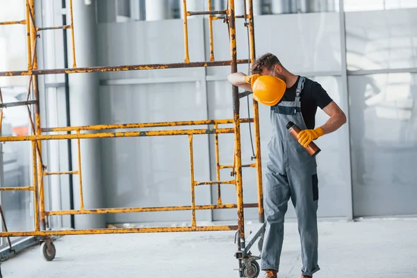 İnşaatın yanındaki gri üniformalı adam modern büyük ofiste gündüz vakti kapalı bir yerde mola veriyor..