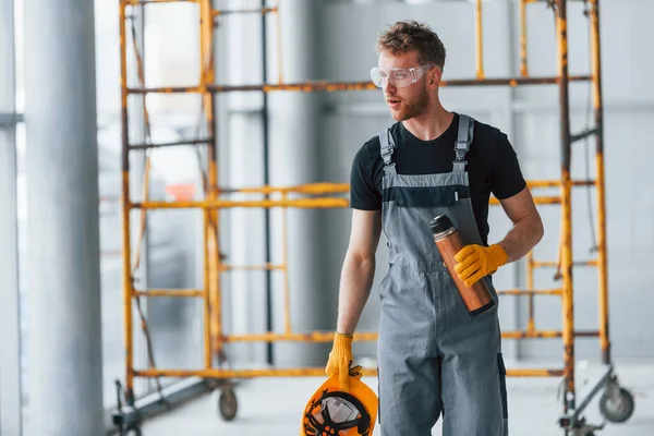 İnşaatın yanındaki gri üniformalı adam modern büyük ofiste gündüz vakti kapalı bir yerde mola veriyor..