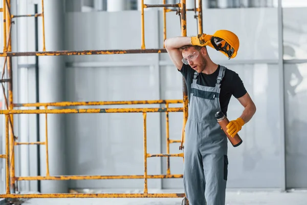 İnşaatın yanındaki gri üniformalı adam modern büyük ofiste gündüz vakti kapalı bir yerde mola veriyor..