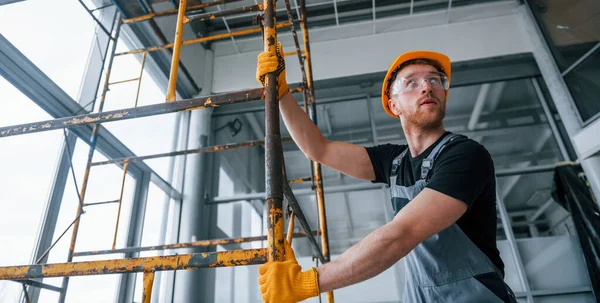Gri üniformalı adam gündüz vakti modern büyük ofiste kapalı alanda inşaat işinde çalışıyor..