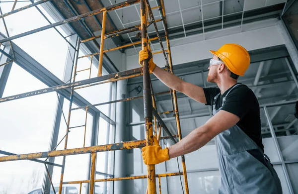 Gri üniformalı adam gündüz vakti modern büyük ofiste kapalı alanda inşaat işinde çalışıyor..