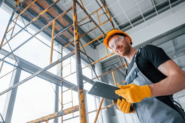 Elinde not defteri olan gri üniformalı bir mühendis modern büyük ofiste gündüzleri kapalı bir yerde çalışıyor..